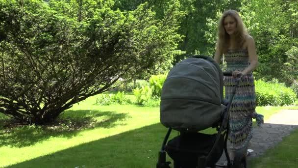 Mother in dress try to send baby to sleep in stroller in garden. 4K — Stock Video
