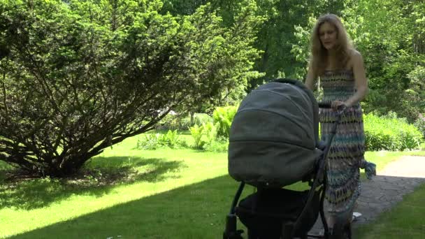 Mutter in Kleid versucht Baby im Kinderwagen im Garten schlafen zu schicken. 4k — Stockvideo