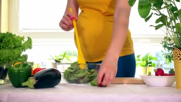 Беременные женский желудок и руки смешивают салат в стеклянной тарелке на столе — стоковое видео