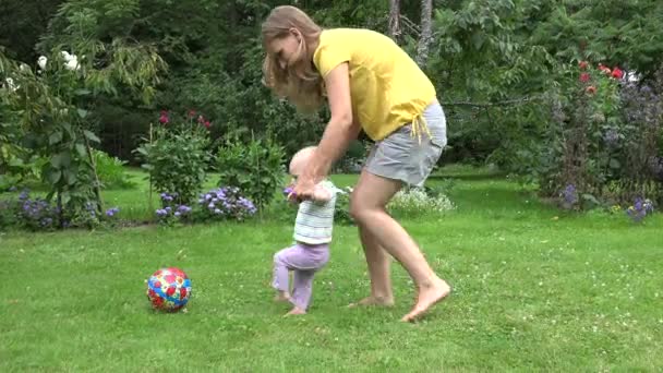 Αξιολάτρευτο μωρό αγόρι κάνοντας τα πρώτα βήματα που πιάνει μπάλα με την υποστήριξη της μητέρας πράσινο γκαζόν. — Αρχείο Βίντεο
