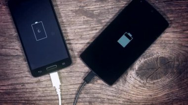 Grunge ahşap arka plan üzerinde şarj iki akıllı telefonlar. Durumunu ekranda.