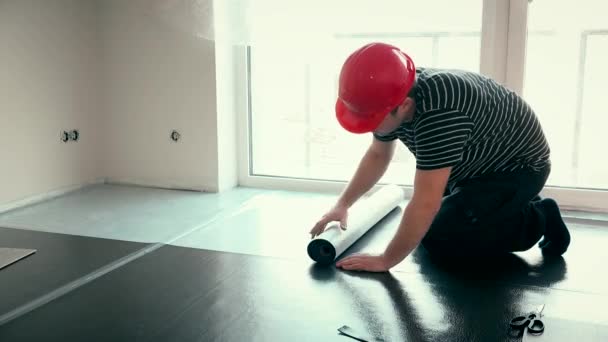 Homem construtor profissional com capacete vermelho leigos esteira underlay deck no novo quarto — Vídeo de Stock