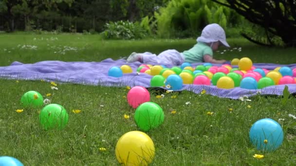 Oskärpa söt baby flicka ha kul mellan färgglada bollar på Pläd i ängen. 4k — Stockvideo