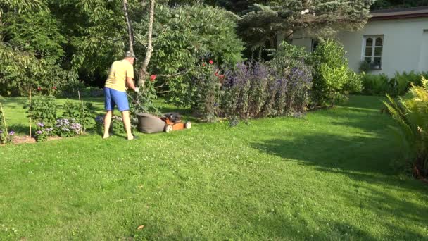 Mann arbeitet mit Rasenmäher in grünem Blumengarten in der Nähe seines Hauses. 4k — Stockvideo