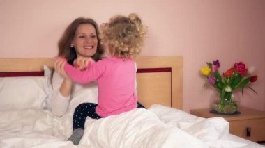 Mutlu anne ve küçük kızı yatağa oturmuş ve oyun
