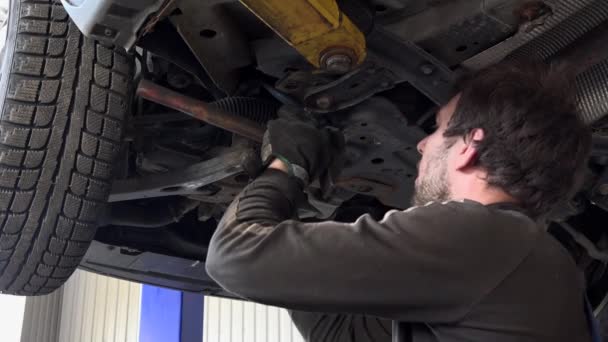 Работник гаража устанавливает новую систему стабилизации колес под поднятым автомобилем . — стоковое видео