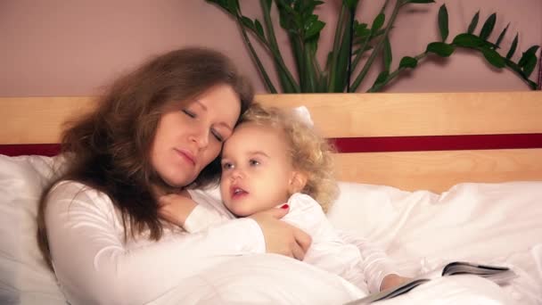 Roztomilá holčička s kudrnatými vlasy, spaní s matkou v bílé posteli obejmeš — Stock video