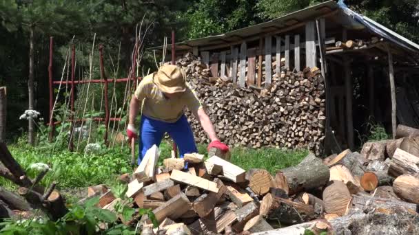Сильный человек рубит дрова топором во дворе деревни. Сезонная работа. 4K — стоковое видео
