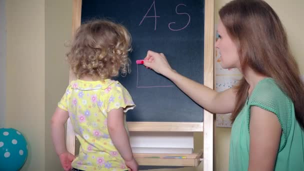 Mulher pintando casa e cartas para criança menina no quadro negro com giz — Vídeo de Stock