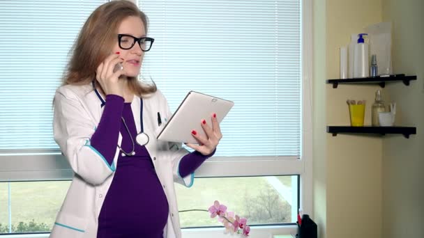 Médica grávida conversando no telefone e usando o computador tablet juntos — Vídeo de Stock