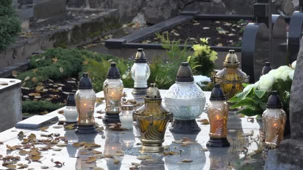 Linternas de velas y hojas de otoño en la tumba de piedra en el cementerio. Primer plano. 4K — Vídeos de Stock