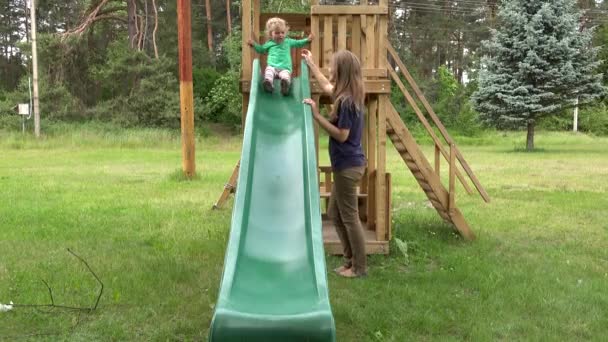 Vorsichtige Mutter hilft ihrer Kleinkind-Tochter auf Spielplatz nach unten zu rutschen.