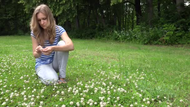 Mujer rubia sentarse en el prado tejer corona cabeza de flores de plantas de trébol. 4K — Vídeos de Stock