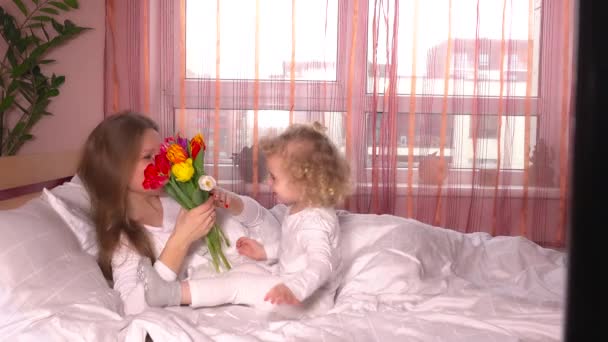 Hija del niño felicita a las mamás y le da flores de tulipán en la cama — Vídeos de Stock