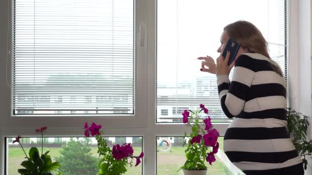 Suspicious pregnant woman calling police on phone while looking through window — Stock Video