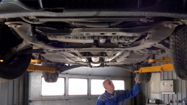 Skilled garage worker examining lifted car. — Stock Video