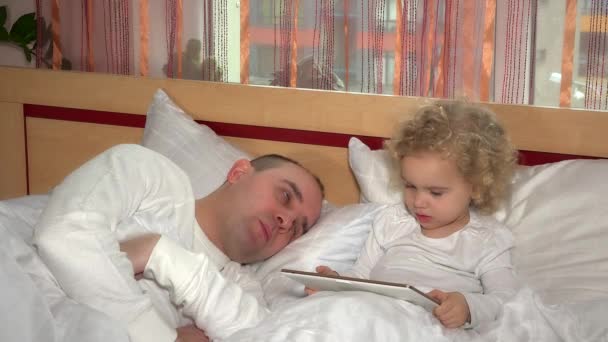 Уставший отец мужчина засыпает, пока малышка дочь смотрит в планшетном компьютере — стоковое видео