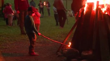 Büyük ateşin önünde sopa ayakta olan küçük çocuk