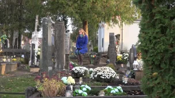 Trieste vrouw zitten op de Bank in de buurt van het graf van echtgenoot vader in begraafplaats. Uitzoomen. 4k — Stockvideo