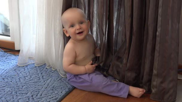 Happy Little baby jongen in de broek spelen in de buurt van gordijn. Glimlachende jongen kijken naar camera — Stockvideo