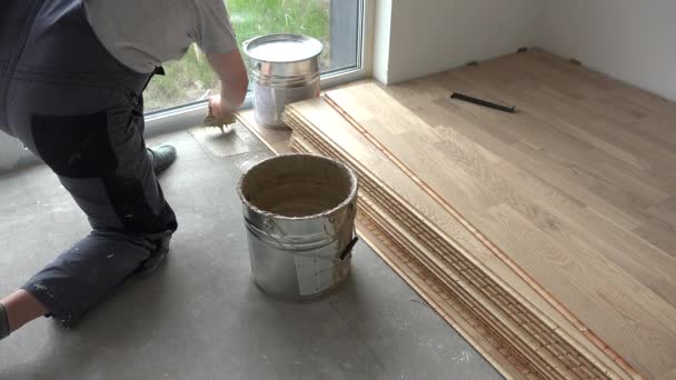 Плотник наносит клей на бетонный пол. Рабочий устанавливает деревянный пол — стоковое видео