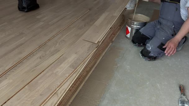 Hombre usando espátula para aplicar pegamento de tabla de parquet sobre hormigón — Vídeos de Stock