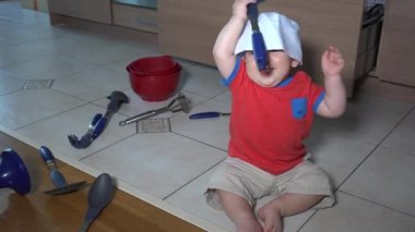 Mutfakta tek başına oynayan küçük çocuk. Yerde oturan şef şapka çocuk almak