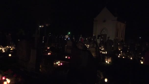 Personnes chrétiennes marchent et prient entre les bougies lumière dans le cimetière la nuit. 4K — Video