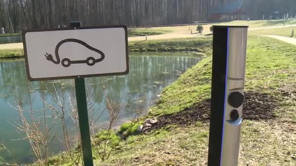 Σταθμός φόρτισης ηλεκτρικού αυτοκινήτου με πινακίδα και υποδοχή κοντά στη λίμνη — Αρχείο Βίντεο