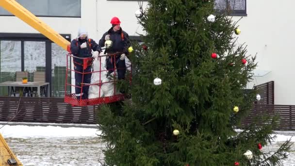Travailleurs hommes sur grue suspendus boules colorées sur l'arbre de Noël dans le quartier urbain — Video