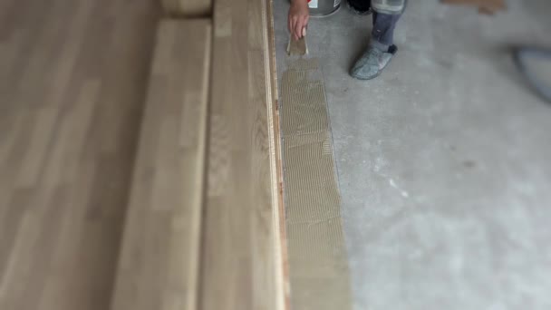 El trabajador unta la cola en el suelo de hormigón en el apartamento nuevo. Pisos de madera — Vídeos de Stock