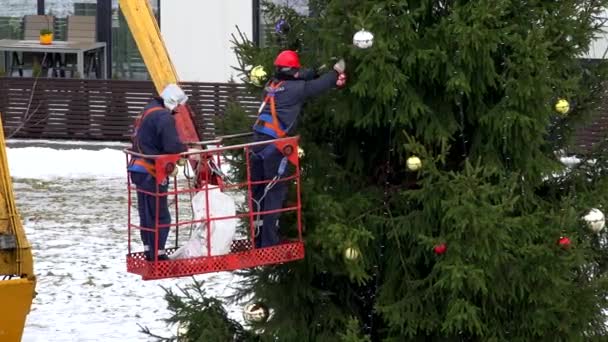Mężczyźni w dźwigu powiesić duże kolorowe kulki zabawki na zewnątrz Choinka — Wideo stockowe