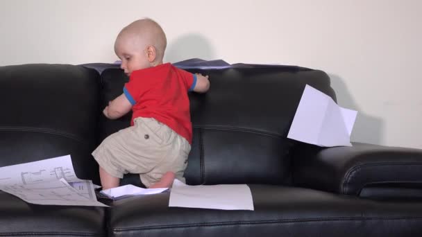 Niño activo jugando con documentos en el sofá — Vídeos de Stock