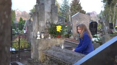 Diz çöküp mezarlıktaki mezarın yanında dua eden üzgün genç bir kadın. 4k
