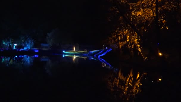 Φωτισμό Φεστιβάλ πολύχρωμο φως κοντά στη λίμνη και τους ανθρώπους τη νύχτα. Πανόραμα. 4K — Αρχείο Βίντεο