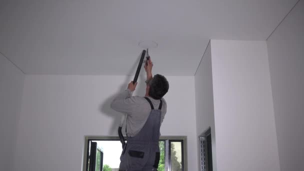 Worker man saw round hole in plasterboard ceiling. Piece of gypsum fall on face — Stock Video