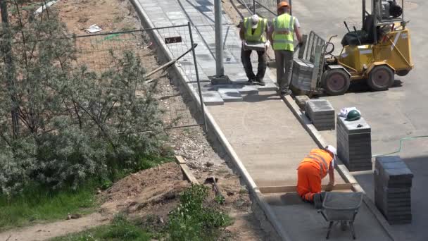 Os trabalhadores preparam a base do solo para a calçada e pavimentar telhas leigas. 4K — Vídeo de Stock