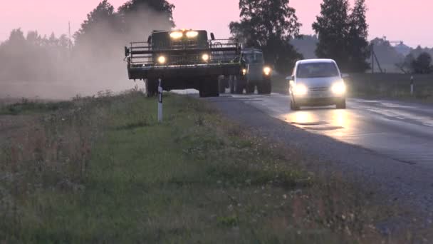 Автомобили обгоняют тяжелый комбайн, едущий по сельской дороге между полями на закате. 4K — стоковое видео