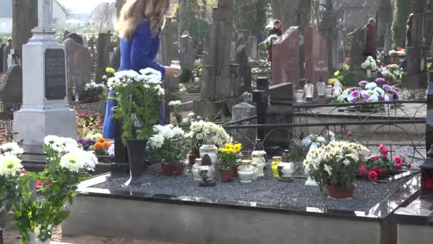 Jeune femme blonde a mis la bougie sur la tombe après la perte du père du mari dans le cimetière. 4K — Video