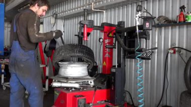 Kirli tamirci araba servisinde lastik değiştiriyor. Lastik rotasyon makinesi