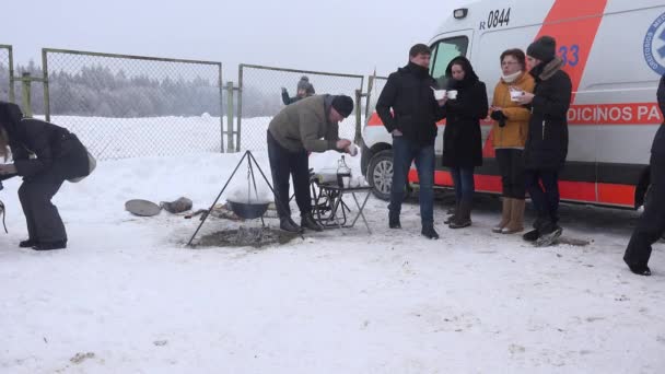 As pessoas comem a sopa quente perto do pote no fogo ao ar livre no inverno frio. 4K — Vídeo de Stock
