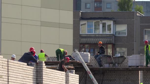 Equipe construtor que estabelece parede de tijolo de concreto branco. Trabalhador fumando cigarro — Vídeo de Stock