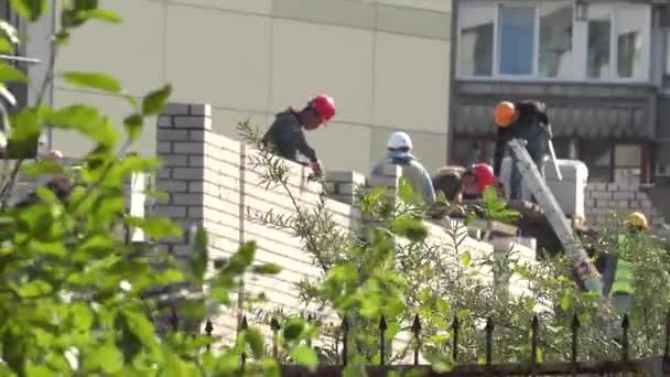 熟练的建筑工人在树木和栅栏包围的建筑工地工作 — 图库视频影像