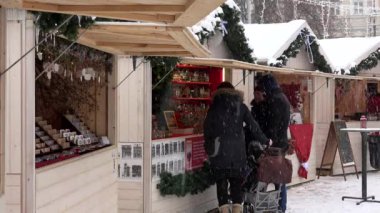 İnsanlar Noel kasabası fuar büfesinde hediyelik eşya yiyecek ve içecek satın alıyorlar. Kar fırtınası
