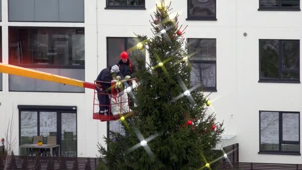 Gemeentelijke werknemers op kraan versieren kerstboom. Dramatische kleurgradatie — Stockvideo