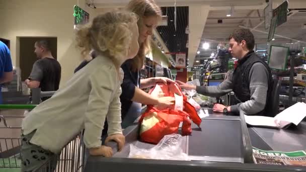 Kasserer checker mand læse varer stregkoder og kunde kvinde sætte varer i pose – Stock-video
