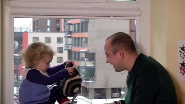 Man with child measure warm winter hats near window. Snowstorm — Stock Video