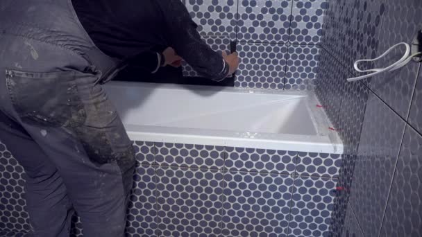Mann legt Fliesen auf Badewannenseite im Badezimmer an — Stockvideo