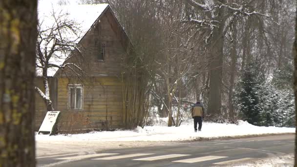 Εγκαταλελειμμένο ξύλινο σπίτι και ο άνθρωπος που περπατάει μέσα από χιονισμένο μονοπάτι το χειμώνα — Αρχείο Βίντεο