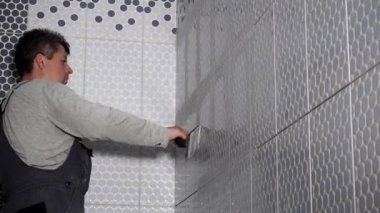İşçi banyodaki duvar kiremitlerine füg koyuyor. Döşemeleri düzenleyen adam